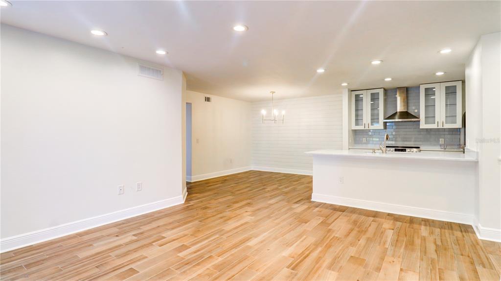 A bright, open-concept kitchen and dining area featuring light wood-look tile flooring and white walls — 9481 HIGHLAND OAK DRIVE UNIT 1001, TAMPA, FL
