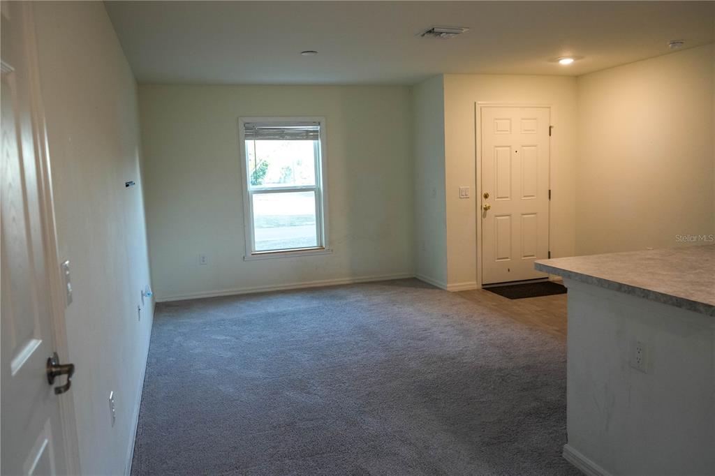 A carpeted living room features a window, a white front door, and a kitchen counter — 22226 STATE AVENUE, PORT CHARLOTTE, FL