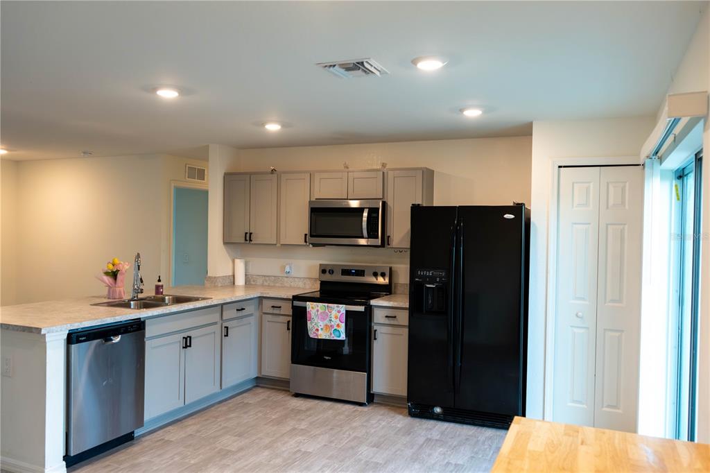 A kitchen features grey cabinets, stainless steel appliances, a black refrigerator, and light-colored countertops — 22226 STATE AVENUE, PORT CHARLOTTE, FL