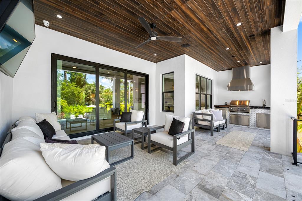 A covered patio features a wood-plank ceiling, outdoor kitchen, and modern seating on stone flooring — 2623 S PARKVIEW STREET, TAMPA, FL