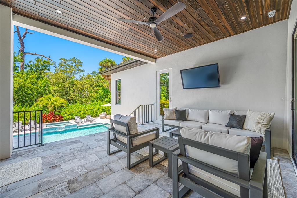 A covered patio features a stone floor, outdoor seating, a wall-mounted television, and a swimming pool — 2623 S PARKVIEW STREET, TAMPA, FL