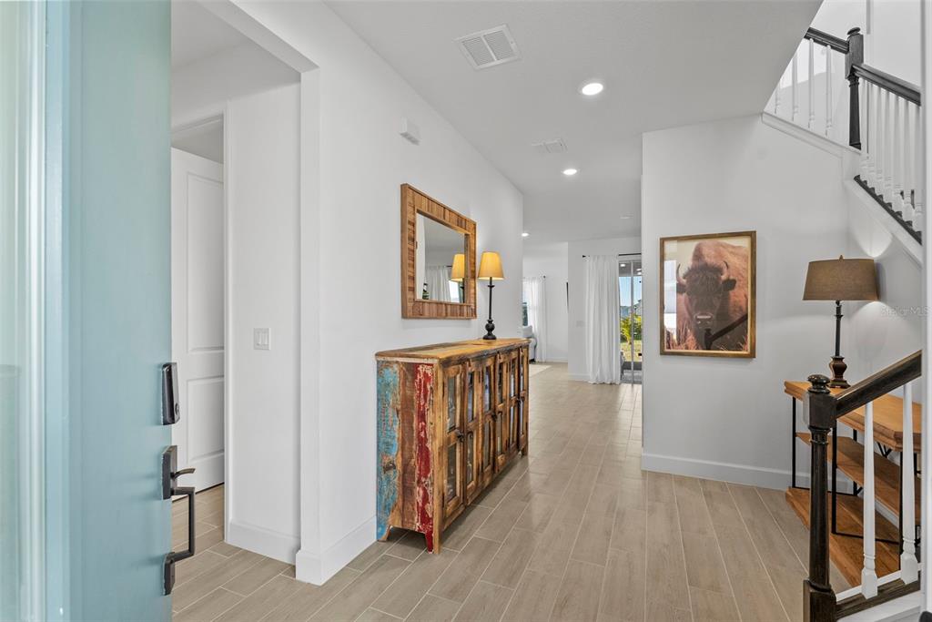 An entryway features light wood-look tile flooring, a rustic wooden console table, and a staircase — 6026 JENSEN VIEW AVENUE, APOLLO BEACH, FL