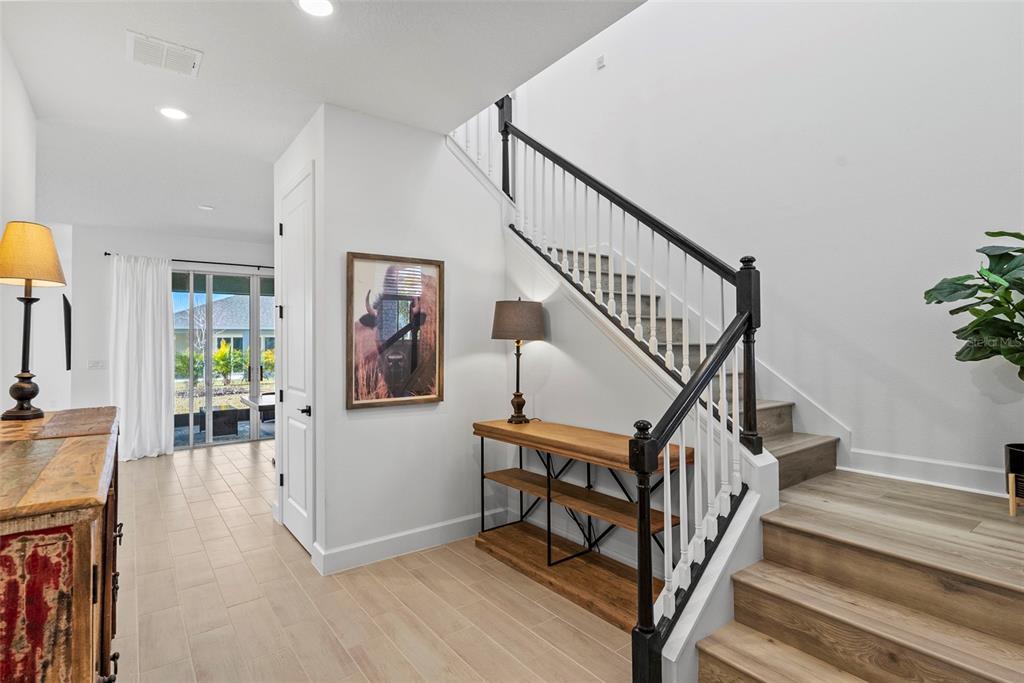 A bright entryway features a wooden staircase with black railings, tile flooring, and a console table — 6026 JENSEN VIEW AVENUE, APOLLO BEACH, FL