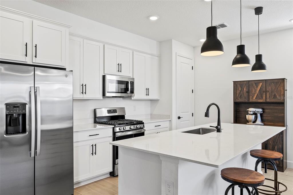 A modern kitchen features white cabinets, stainless steel appliances, a quartz island, and pendant lighting — 6026 JENSEN VIEW AVENUE, APOLLO BEACH, FL