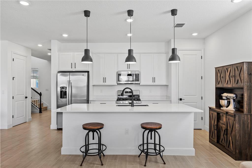A modern kitchen features white cabinetry, a central island with bar stools, and stainless appliances — 6026 JENSEN VIEW AVENUE, APOLLO BEACH, FL
