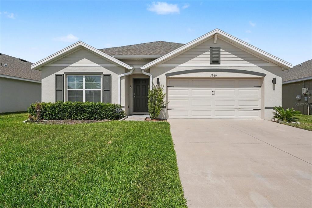 A single-story suburban house with a beige stucco exterior, a two-car garage, and a lawn — 7980 BROAD POINTE DRIVE, ZEPHYRHILLS, FL