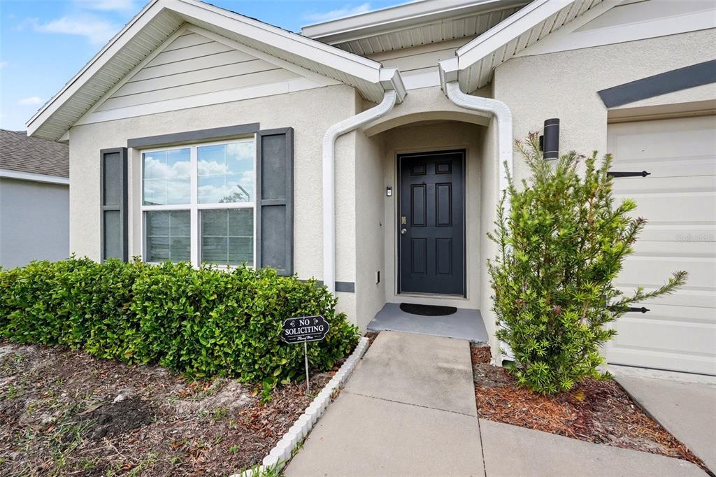 The exterior of a house features a dark front door, a walkway, and green landscaping — 7980 BROAD POINTE DRIVE, ZEPHYRHILLS, FL