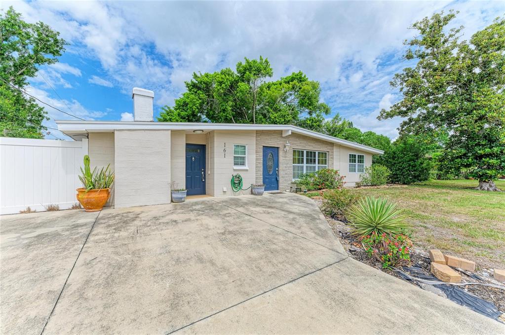 The exterior of a single-story house features a concrete driveway, two blue doors, and stone siding — 161 SUNTAN AVENUE, SARASOTA, FL