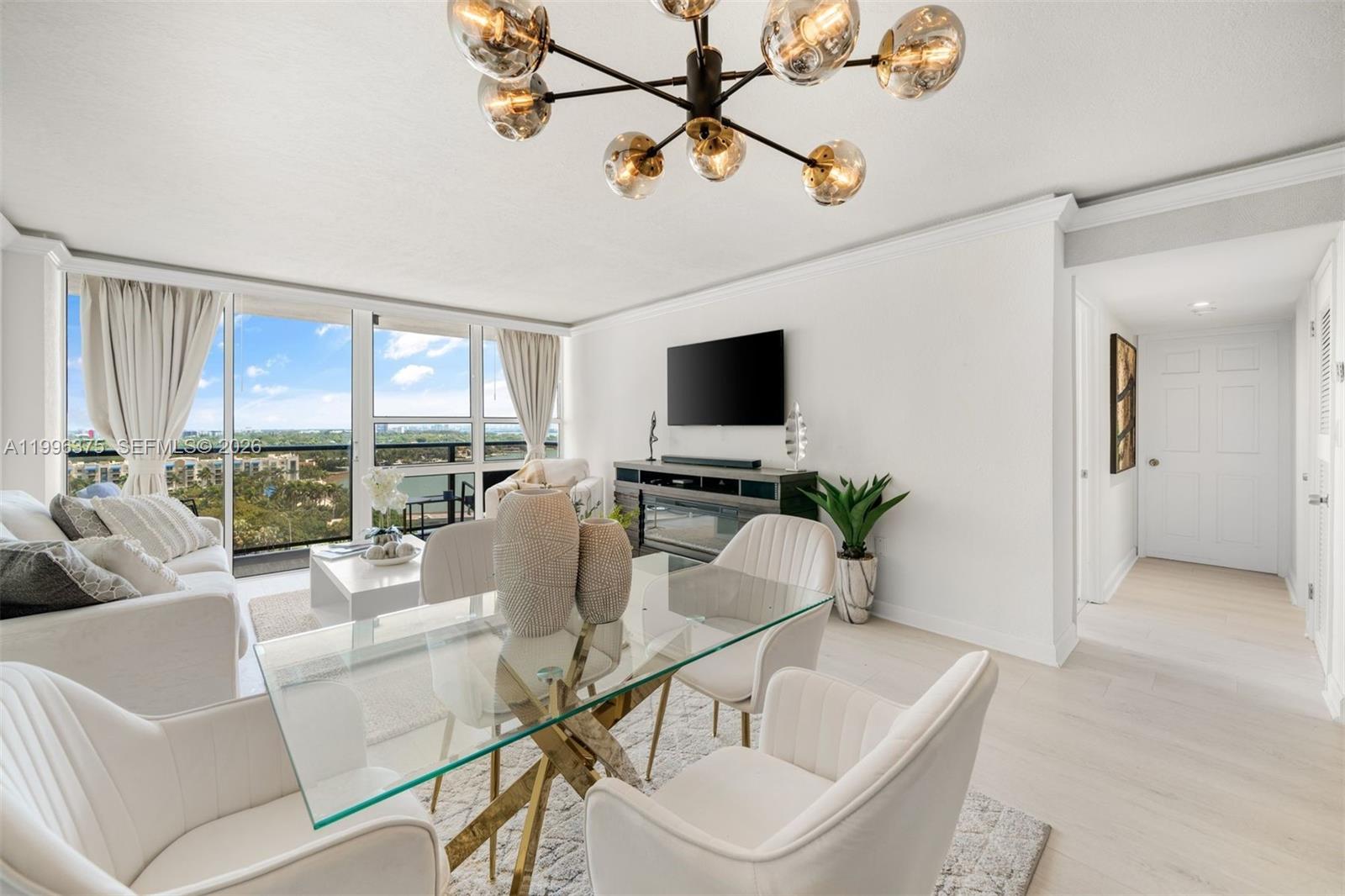 A bright living and dining area features a glass table, modern chandelier, and balcony view — 600 NE 36th ST # 1414, Miami FL 33137, MIAMI, FL