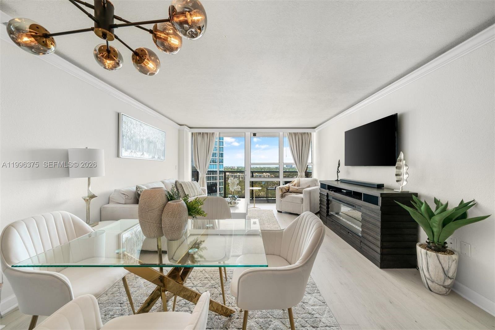 A living and dining area features a glass table, modern chandelier, and balcony view — 600 NE 36th ST # 1414, Miami FL 33137, MIAMI, FL