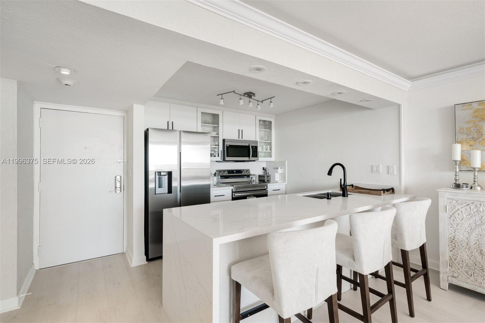 A modern kitchen features white cabinetry, stainless steel appliances, and a waterfall-edge quartz island — 600 NE 36th ST # 1414, Miami FL 33137, MIAMI, FL