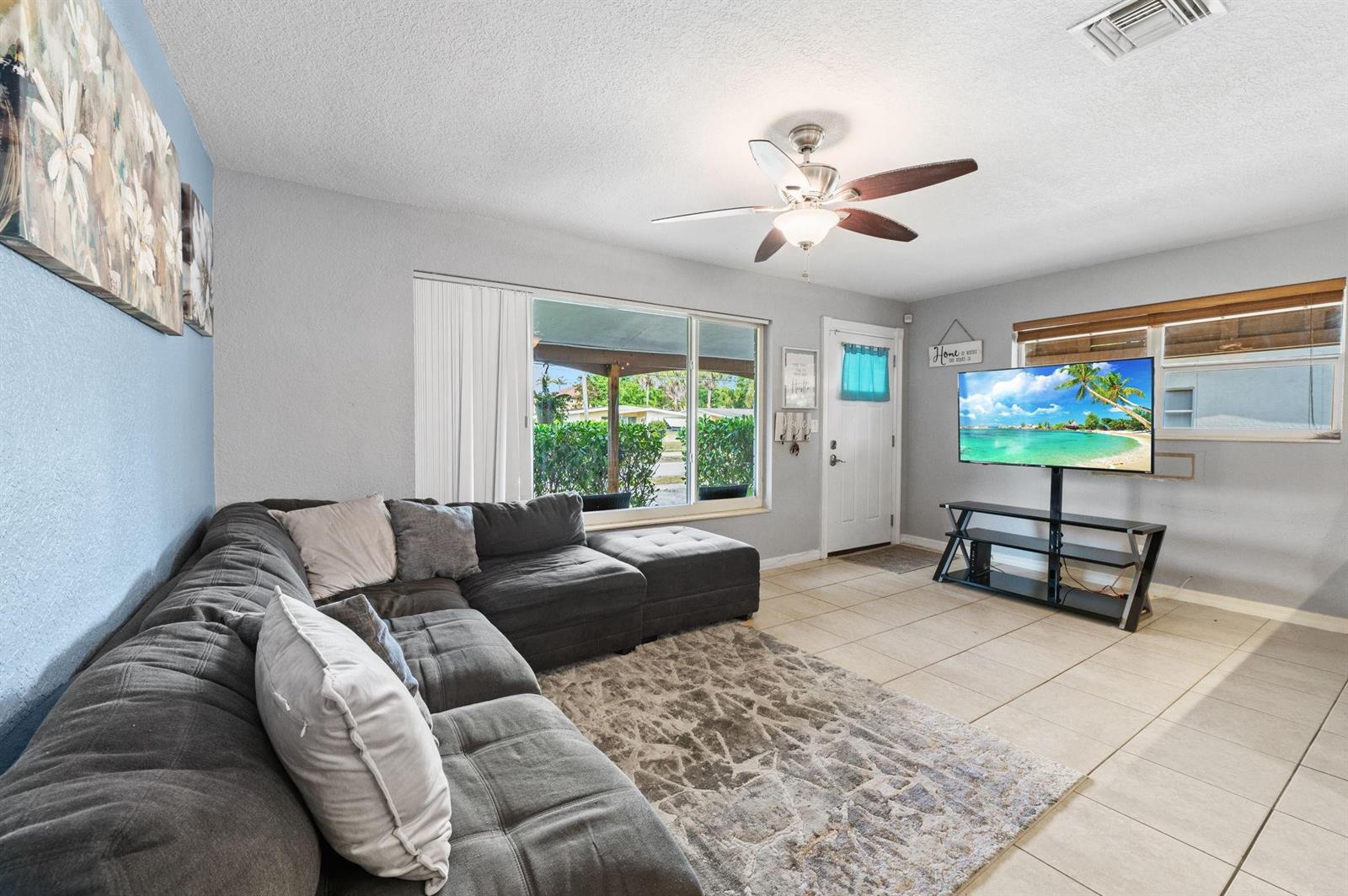 A living room features a gray sectional sofa, a television on a stand, and tile flooring — 5554 SW 6th Street, Margate FL 33068, MARGATE, FL