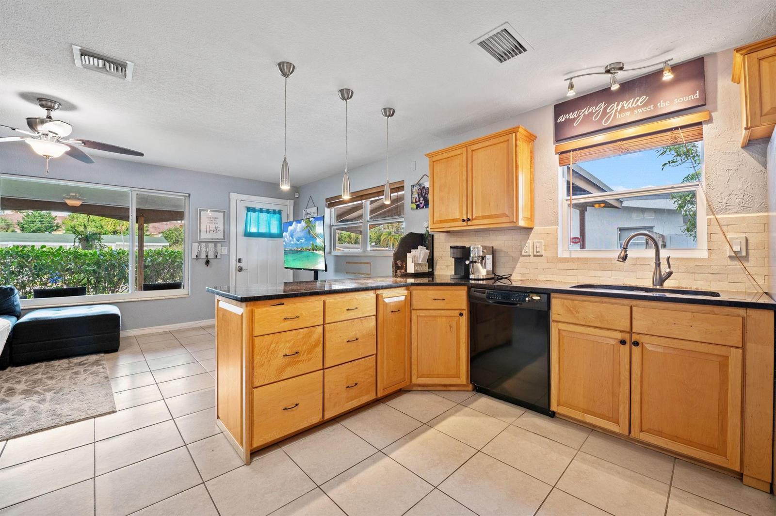 A kitchen features light wood cabinets, black countertops, tile flooring, and a breakfast bar island — 5554 SW 6th Street, Margate FL 33068, MARGATE, FL