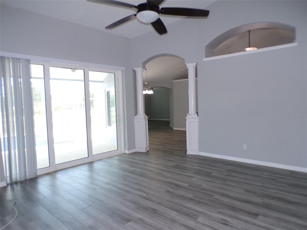 A living room features gray wood-look flooring, white columns, sliding glass doors, and a ceiling fan — 1077 ROTONDA CIRCLE, ROTONDA WEST, FL