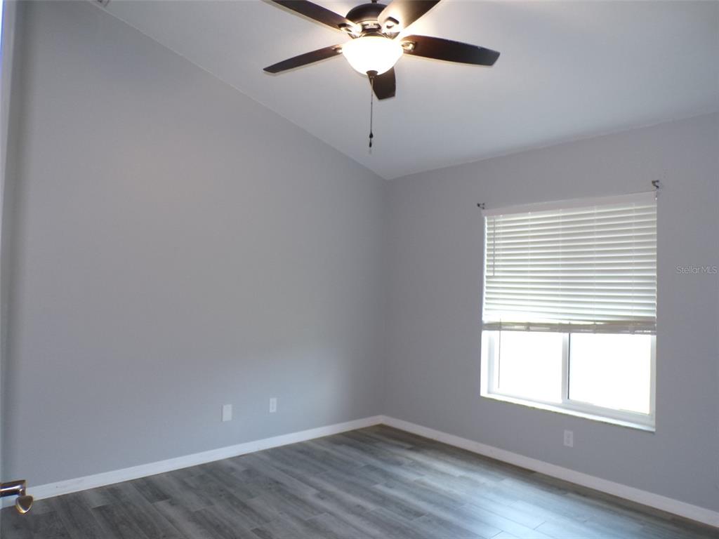 An empty bedroom features light gray walls, wood-look flooring, a ceiling fan, and a window — 1077 ROTONDA CIRCLE, ROTONDA WEST, FL
