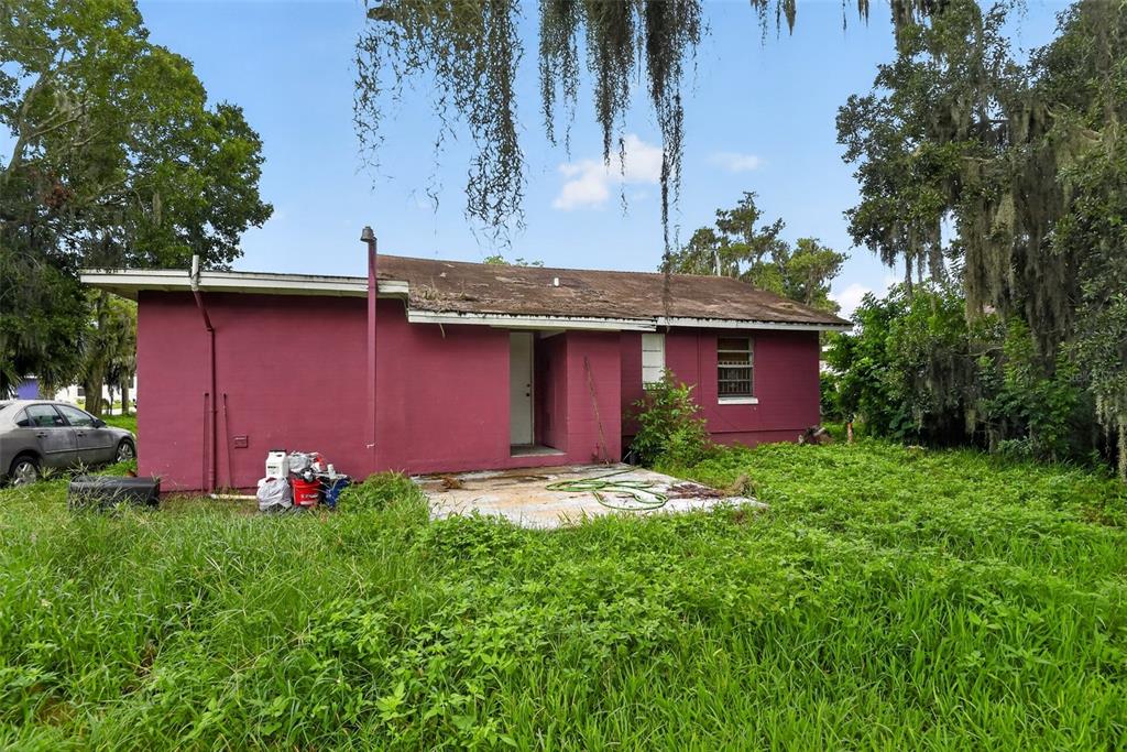 A pink, single-story house with a flat roof is surrounded by overgrown grass and trees — 505 FULTON STREET, DAYTONA BEACH, FL
