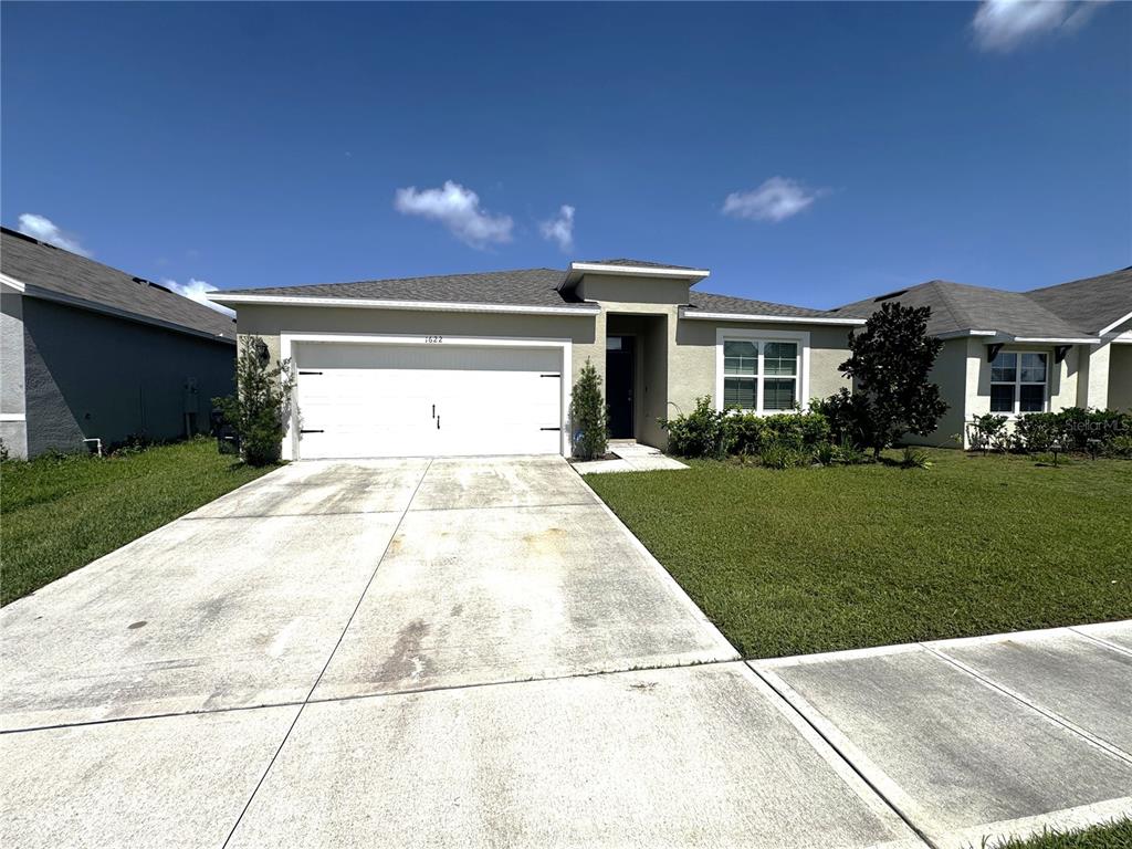 A single-story house with a white garage door, tan stucco exterior, and a concrete driveway — 1622 REDDISH EGRET COURT, DAVENPORT, FL