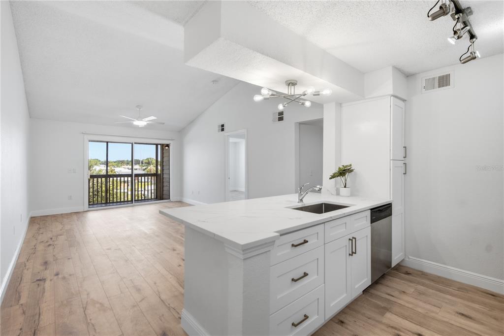 A kitchen with white cabinets and a quartz island overlooks a living area with balcony access — 2500 WINDING CREEK BOULEVARD UNIT F305, CLEARWATER, FL