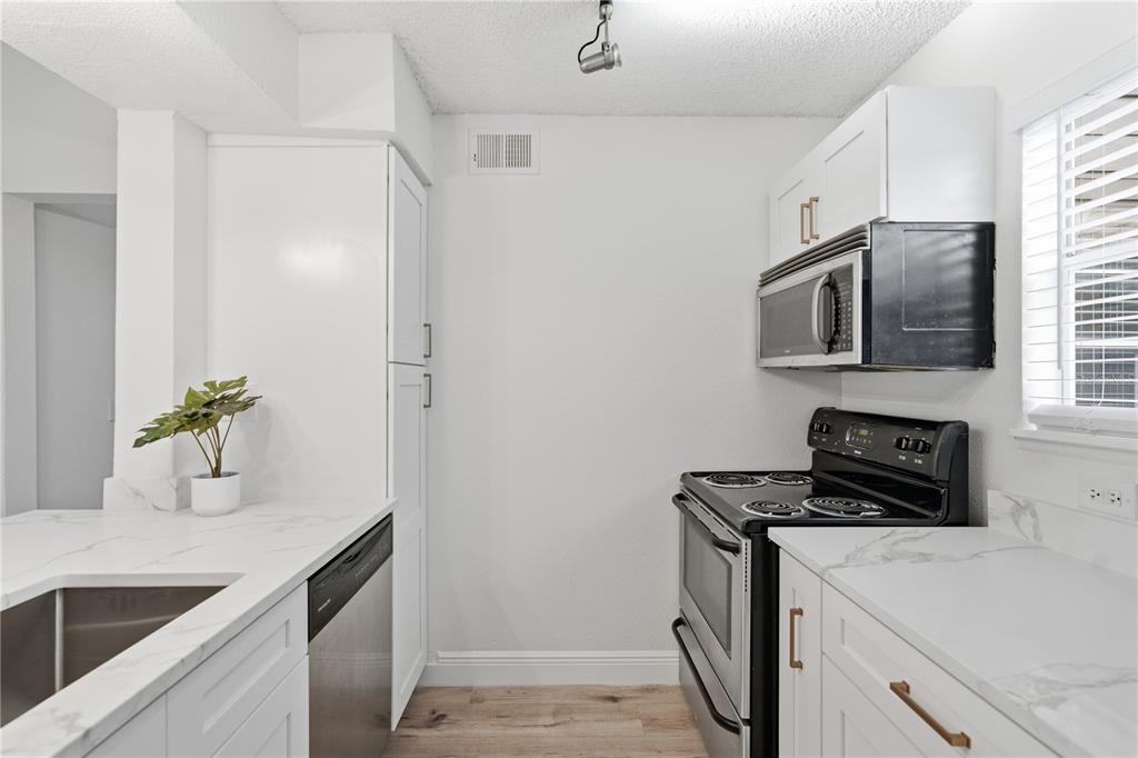 A kitchen features white cabinets, marble-look countertops, stainless steel appliances, and light wood flooring — 2500 WINDING CREEK BOULEVARD UNIT F305, CLEARWATER, FL
