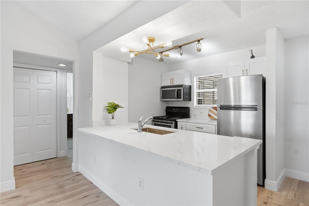 A kitchen features white cabinets, a marble-look countertop island with a sink, and stainless appliances — 2500 WINDING CREEK BOULEVARD UNIT F305, CLEARWATER, FL