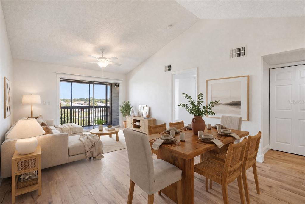 A bright living and dining area features vaulted ceilings, light wood flooring, and a balcony — 2500 WINDING CREEK BOULEVARD UNIT F305, CLEARWATER, FL