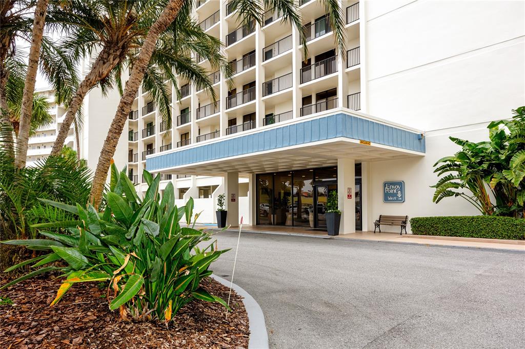 The exterior of a multi-story apartment building features a covered entrance with a blue awning — 7100 SUNSET WAY UNIT 810, ST PETE BEACH, FL