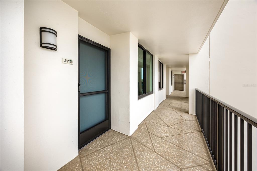 An outdoor apartment hallway features a door labeled 810, a metal railing, and patterned flooring — 7100 SUNSET WAY UNIT 810, ST PETE BEACH, FL