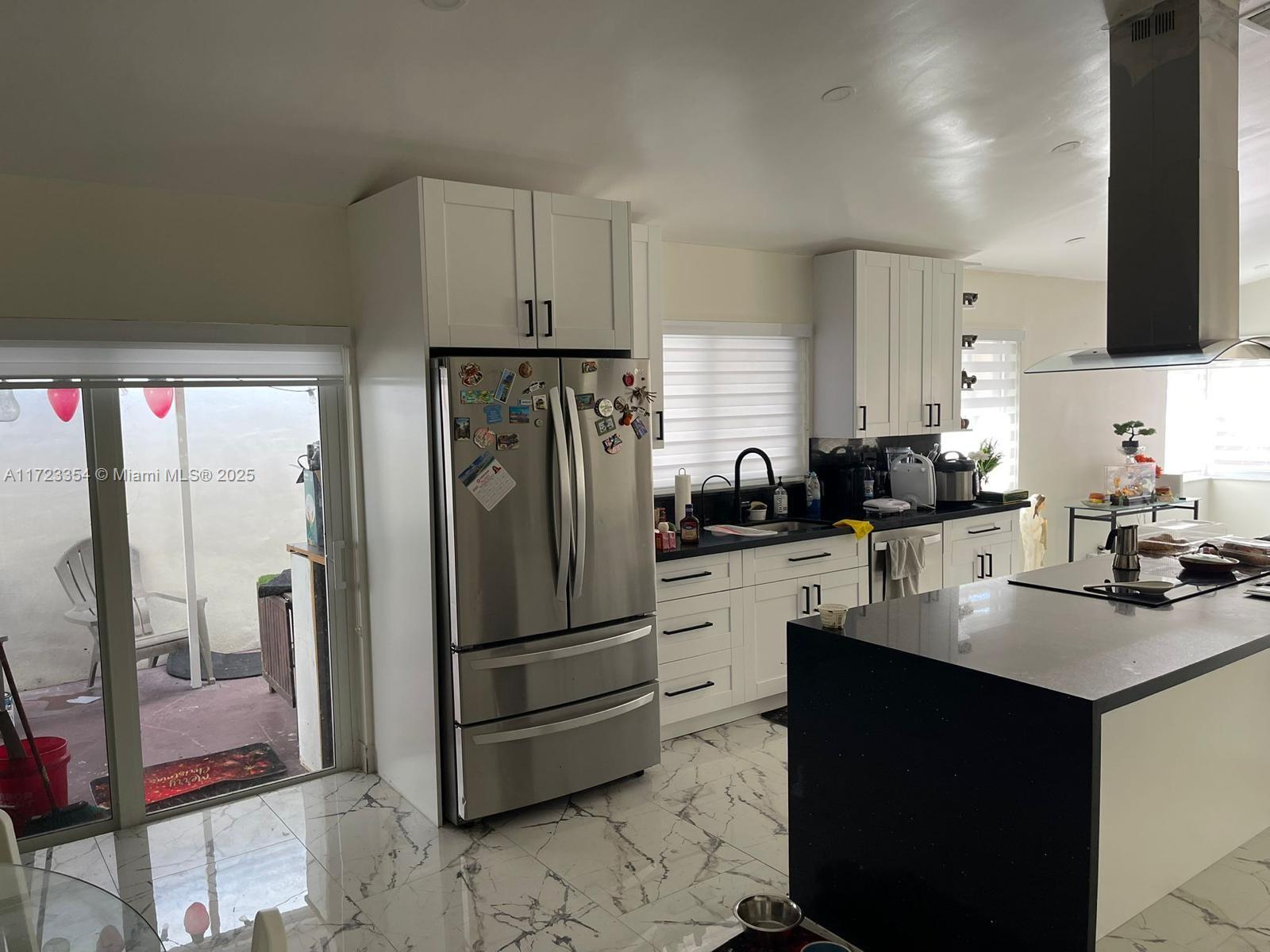 A kitchen features white cabinets, black countertops, a stainless steel refrigerator, and marble-patterned tile flooring — 981 NW 134th Ave, Miami FL 33182, MIAMI, FL