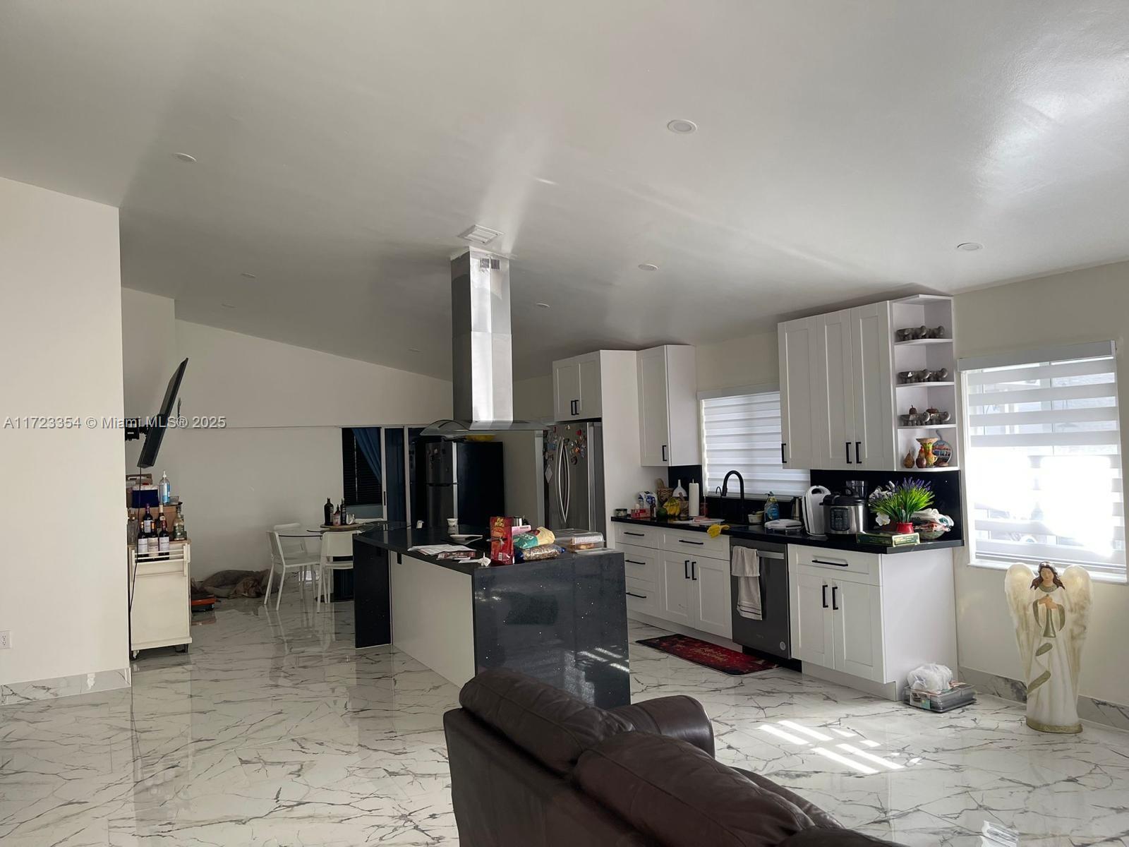A kitchen features white cabinets, a black island, and marble-patterned flooring in an open space — 981 NW 134th Ave, Miami FL 33182, MIAMI, FL