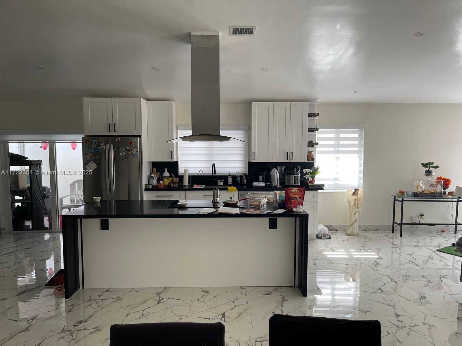 A modern kitchen features white cabinets, a black island, and white marble-patterned tile flooring — 981 NW 134th Ave, Miami FL 33182, MIAMI, FL