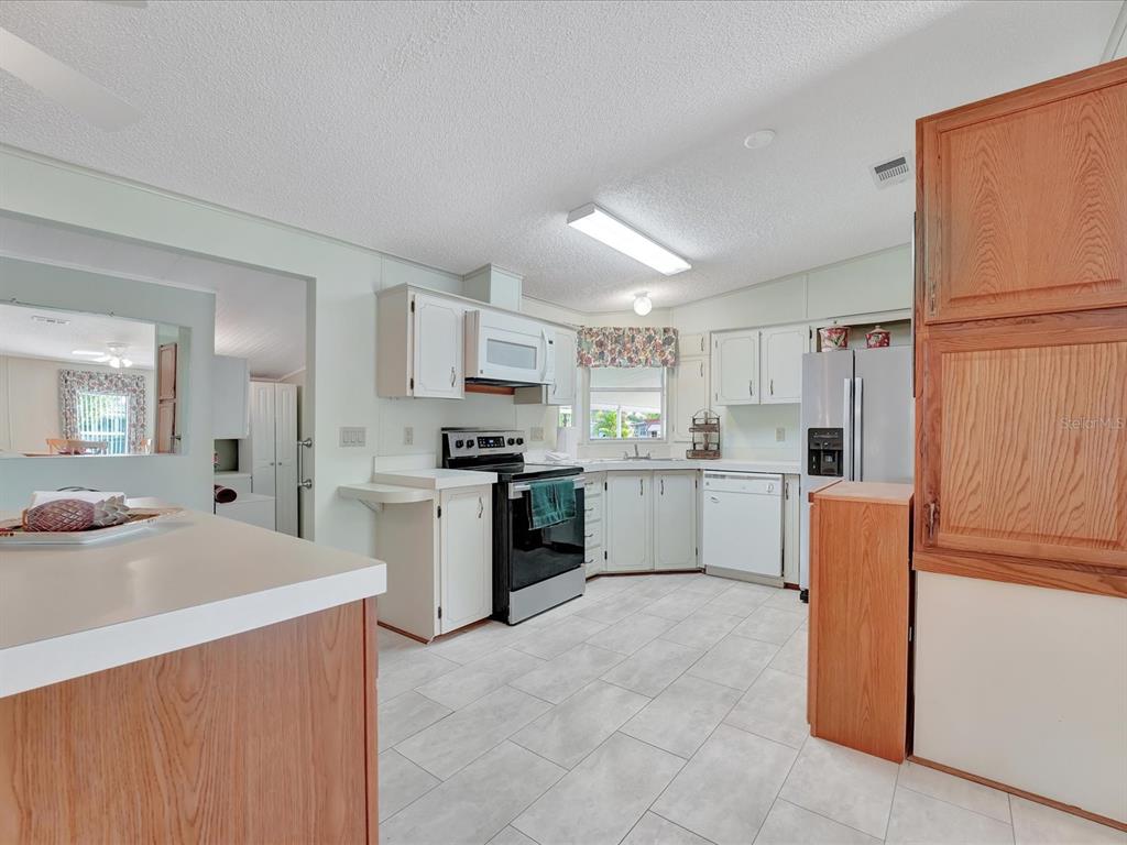 A kitchen features white cabinets, a black stove, a stainless refrigerator, and light tile flooring — 118 SAINT PIERRES WAY, APOLLO BEACH, FL
