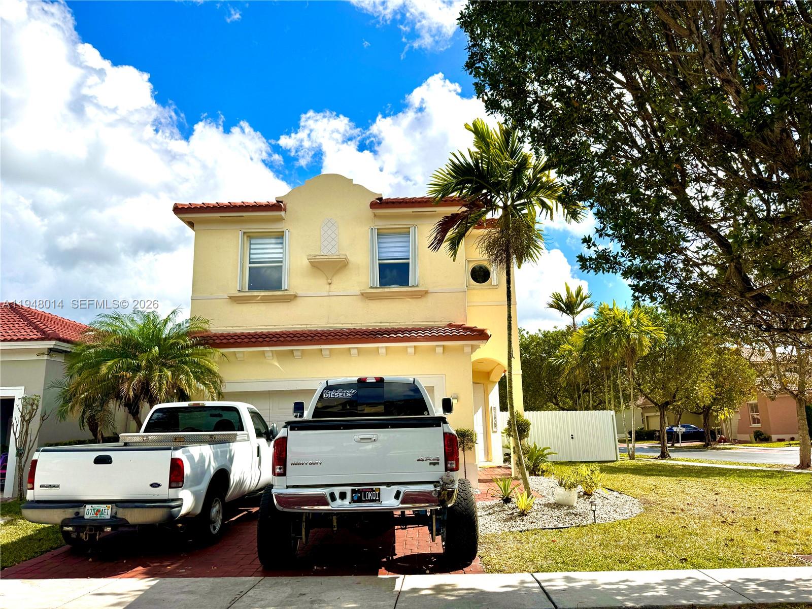 A two-story yellow stucco house with a red tile roof and two parked pickup trucks — 2101 NE 37th Ter, Homestead FL 33033, HOMESTEAD, FL