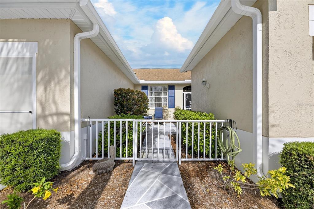 A gated courtyard entrance leads to a front door between two beige exterior walls — 1012 RADISON AVENUE UNIT 12, SUN CITY CENTER, FL