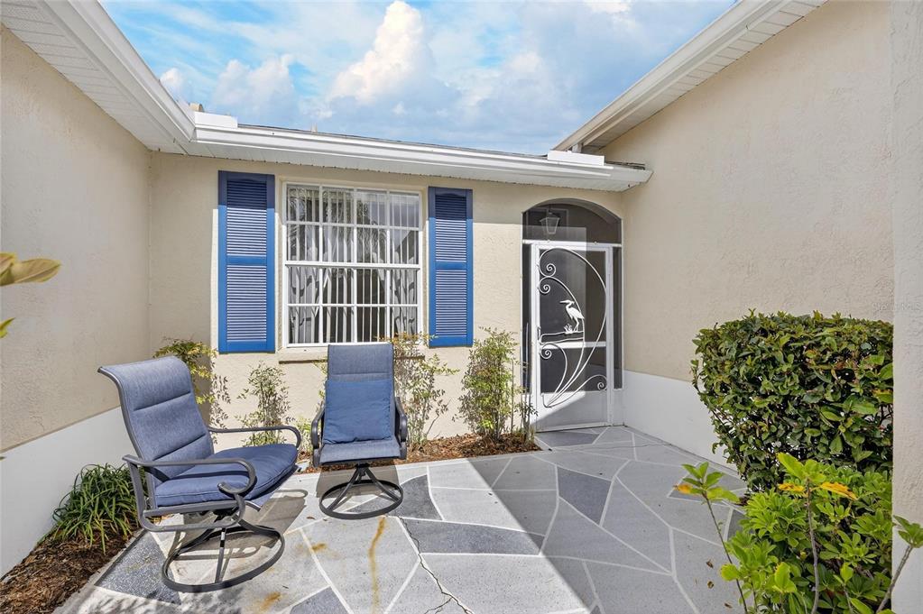A paved patio features two blue chairs, a window with blue shutters, and a screen door — 1012 RADISON AVENUE UNIT 12, SUN CITY CENTER, FL