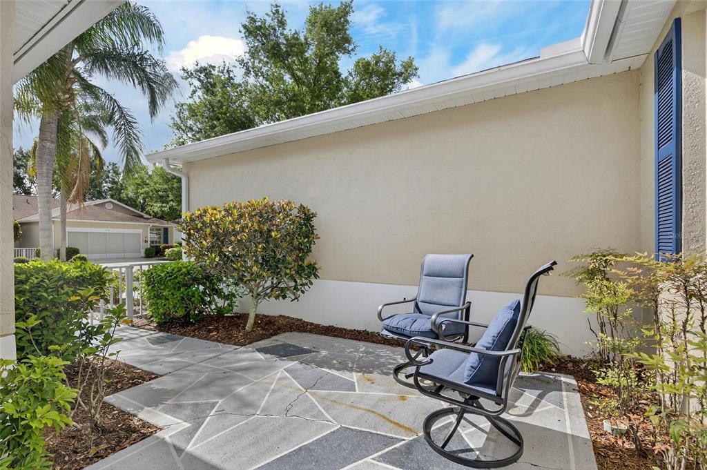 A patio with two chairs sits next to a beige house with blue shutters — 1012 RADISON AVENUE UNIT 12, SUN CITY CENTER, FL