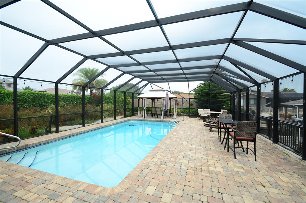 A rectangular swimming pool sits inside a screened-in patio with brick pavers and a gazebo — 58 COMANCHE COURT, PALM COAST, FL
