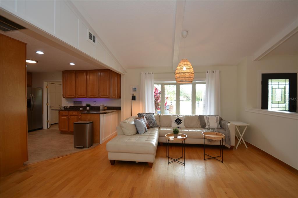 A living room with a white sectional sofa, hardwood floors, and an adjacent open kitchen — 58 COMANCHE COURT, PALM COAST, FL
