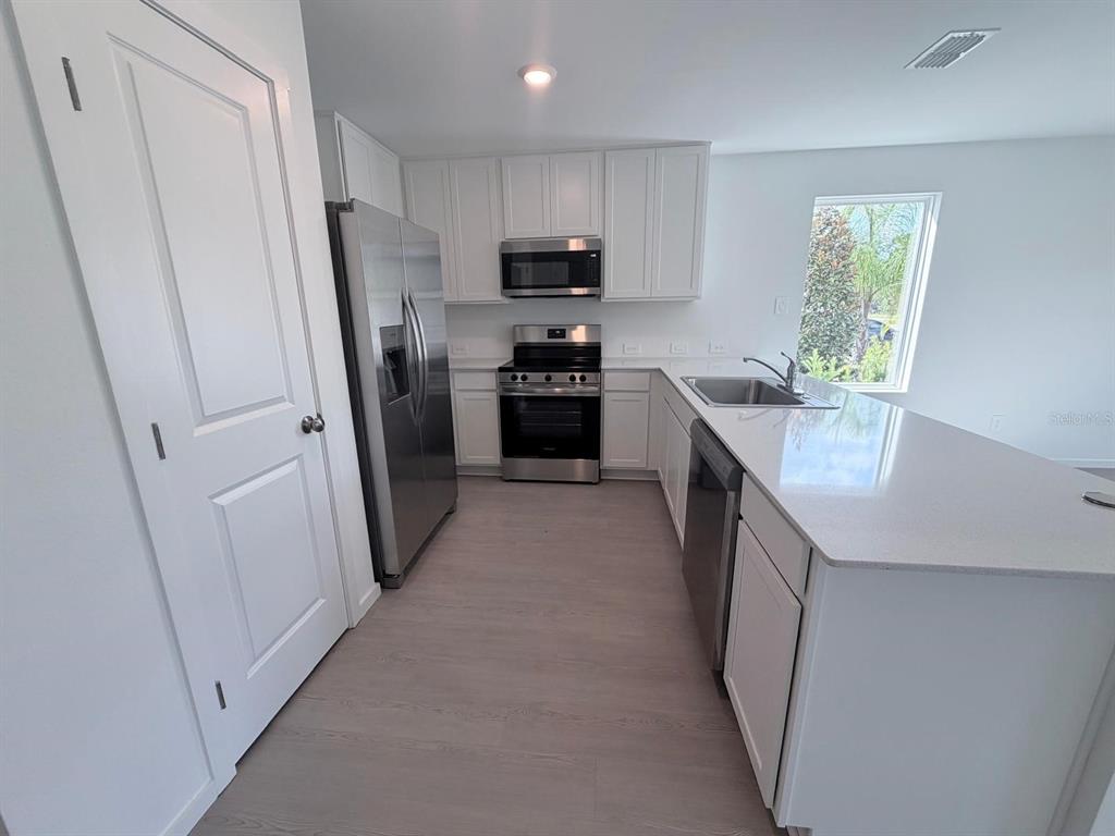 A modern kitchen features white cabinets, stainless steel appliances, and a large quartz-topped island — 1207 ORION STREET, DAVENPORT, FL