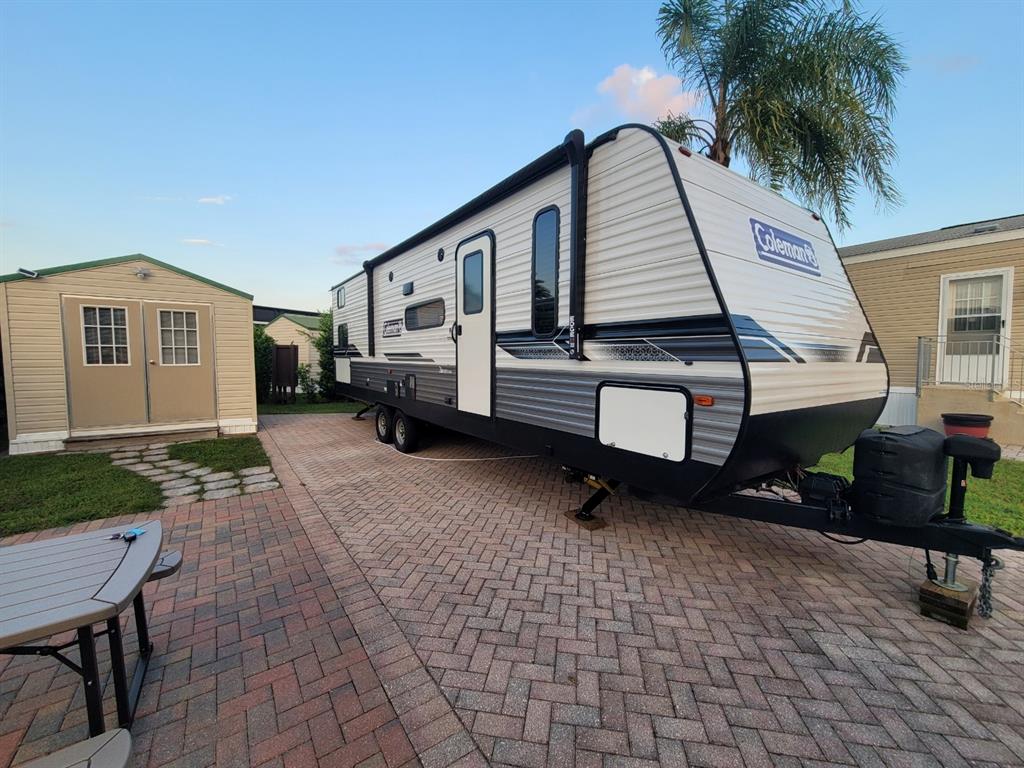 A Coleman travel trailer is parked on a brick paver driveway next to a storage shed — 2418 LIMEWOOD AVENUE UNIT 302, CLERMONT, FL