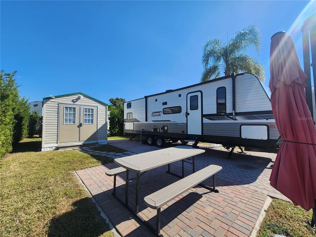 A Coleman travel trailer is parked next to a storage shed on a paved patio — 2418 LIMEWOOD AVENUE UNIT 302, CLERMONT, FL