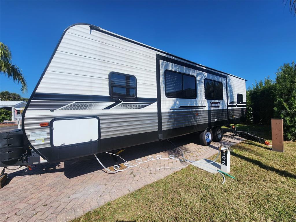 A Coleman travel trailer is parked on a paved driveway next to a grassy lawn — 2418 LIMEWOOD AVENUE UNIT 302, CLERMONT, FL