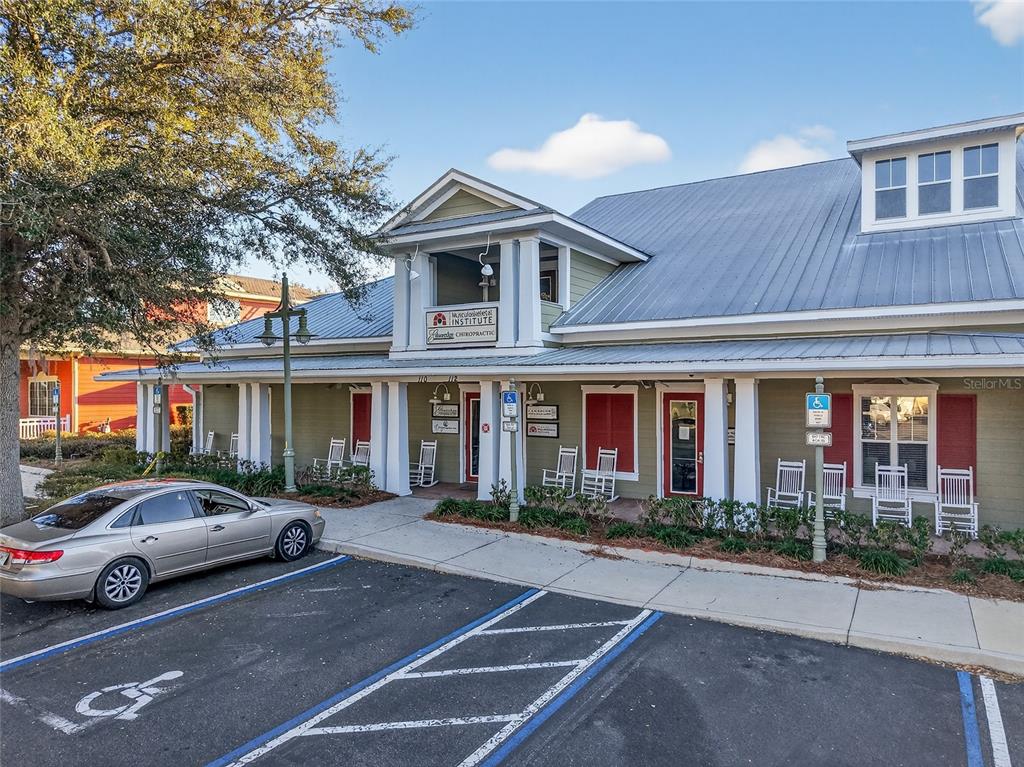 A single-story commercial building with a metal roof and a covered porch with rocking chairs — 910 OLD CAMP ROAD UNIT 110, THE VILLAGES, FL