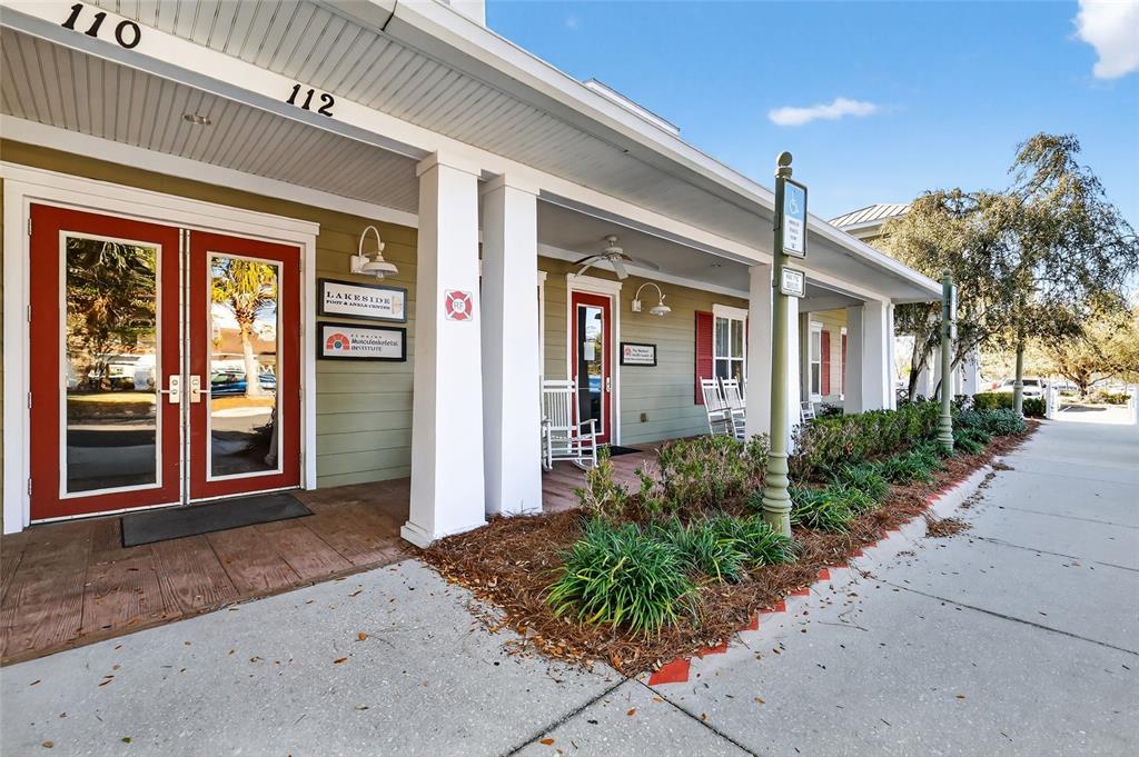 The exterior of a commercial building features a covered porch with rocking chairs and signage — 910 OLD CAMP ROAD UNIT 110, THE VILLAGES, FL