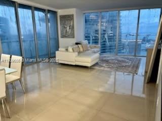 A bright, open-concept living room features large floor-to-ceiling windows, light tile flooring, and a sofa — 465 Brickell Ave # 5402, Miami FL 33131, MIAMI, FL
