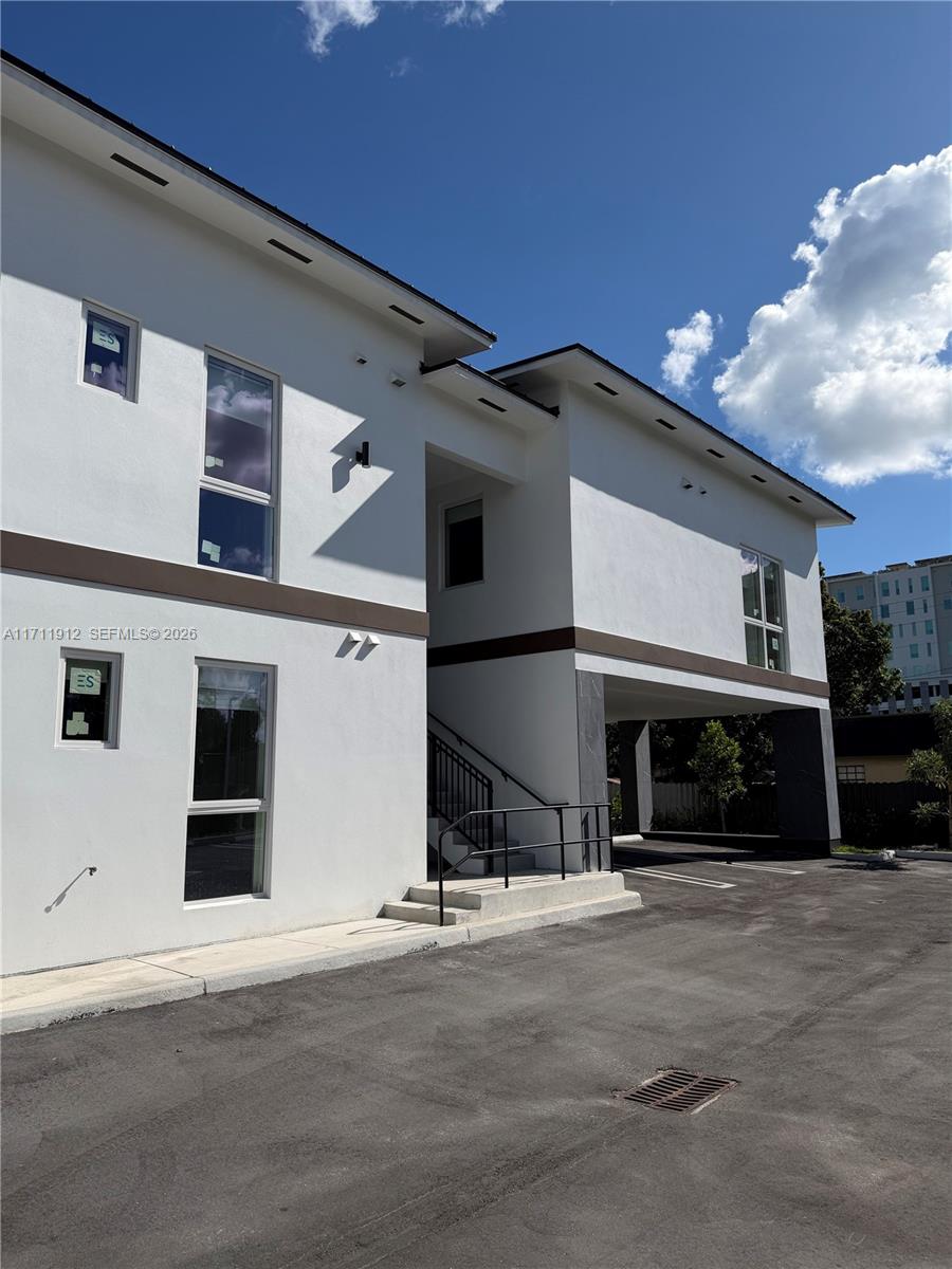 A modern two-story building features white stucco walls, dark trim, and an open ground-level parking area — 210 SE 10th St, Hallandale Beach FL 33009, HALLANDALE BEACH, FL