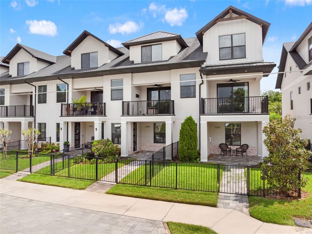 A row of three-story townhomes with white siding, dark roofs, and fenced front yards — 1250 FORMOSA AVENUE, WINTER PARK, FL