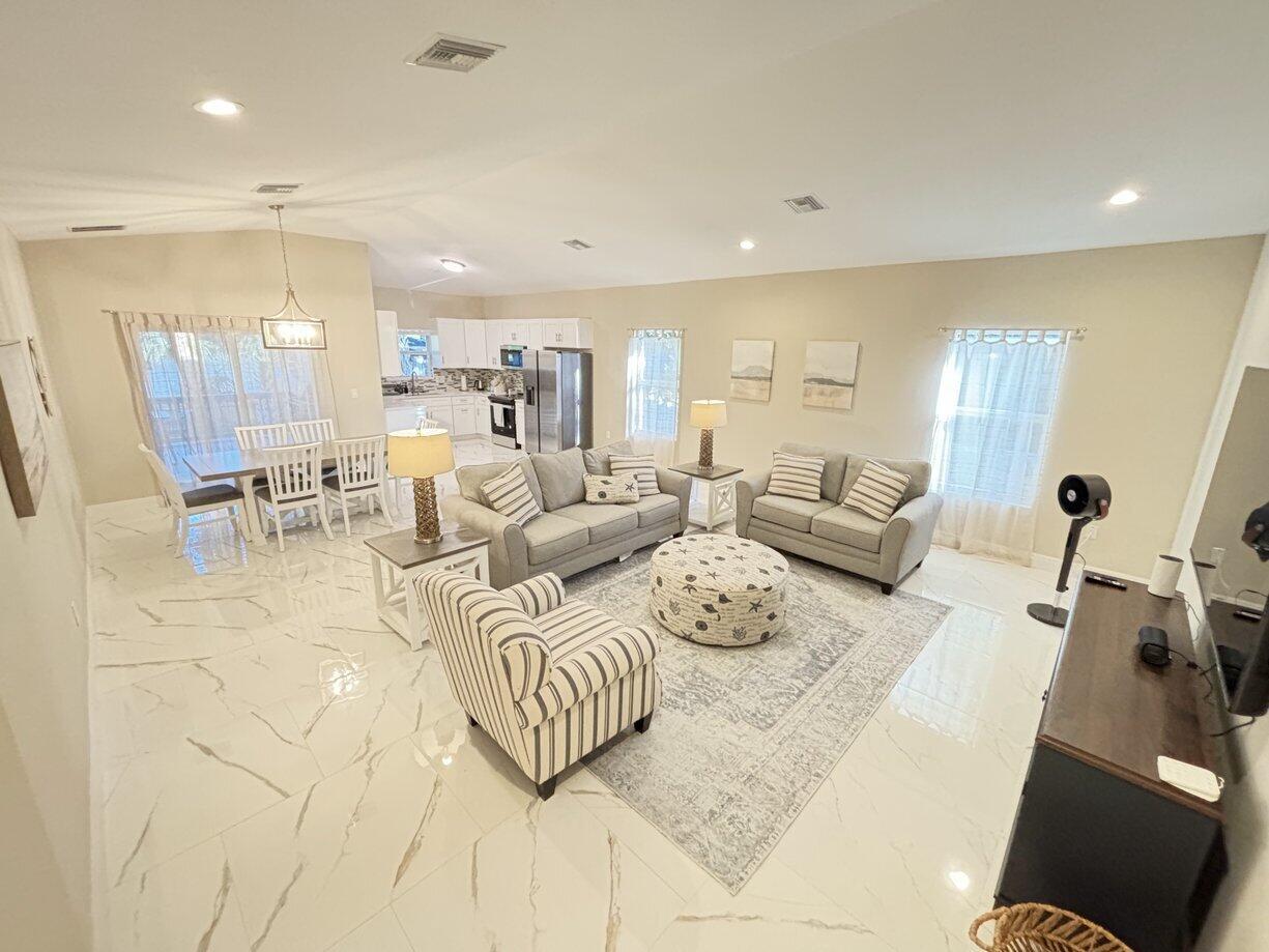 An open-concept living and dining area features white marble-look tile flooring and neutral furniture — 1330 28th Avenue, Vero Beach FL 32960, VERO BEACH, FL