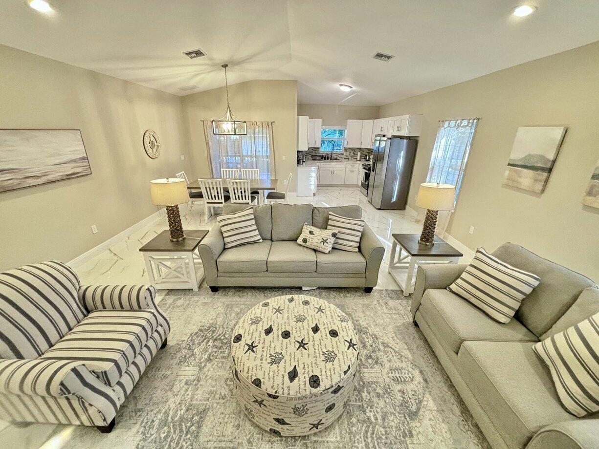 An open-concept living and dining area features light-colored tile flooring and neutral-toned furniture — 1330 28th Avenue, Vero Beach FL 32960, VERO BEACH, FL