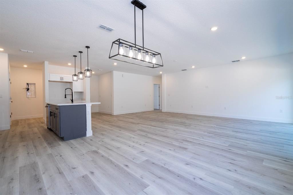 An open-concept living and kitchen area features light wood-look flooring and modern pendant lighting — 3737 BREWSTER ROAD, NORTH PORT, FL