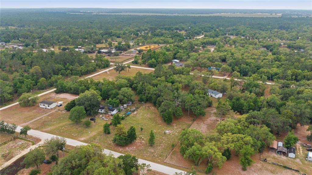 An aerial view shows several houses scattered across a rural, wooded landscape with dirt roads — TBD SE 66 STREET, MORRISTON, FL